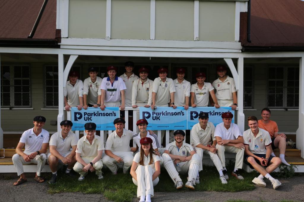 A group of people in cricket uniforms pose for a photo, holding signs that read 'Parkinson's UK'.